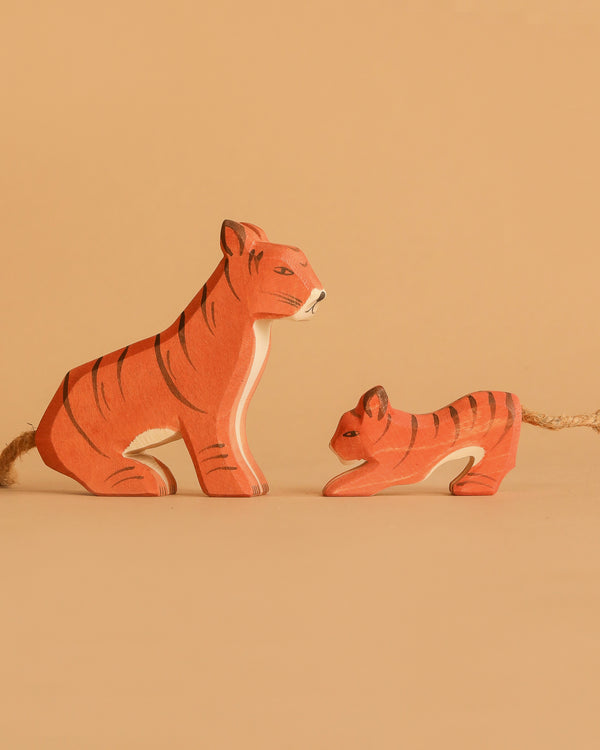 The Ostheimer Handmade Wooden Tiger Set features two painted wooden tiger figurines, one large and one small, with black stripes and rope tails, displayed side by side on a beige background—perfect sustainable toys.