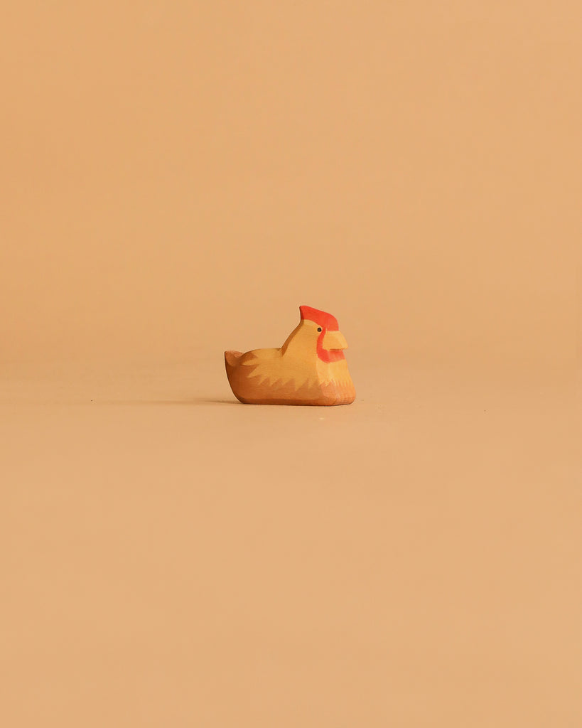 A handcrafted wooden chicken from the Ostheimer Handmade Wooden Farm Animals Set, featuring a red comb, sits on a beige surface—made from sustainably sourced materials in classic Ostheimer style.