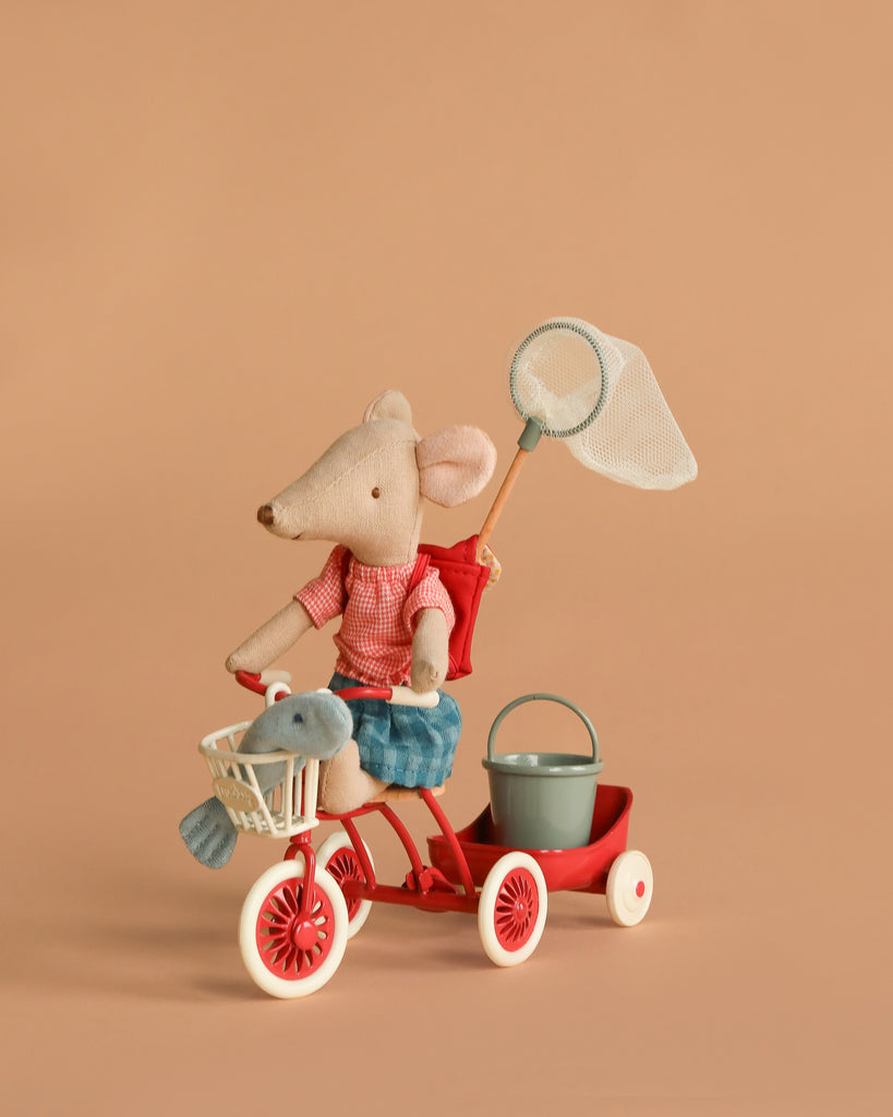 The Maileg Big Sister Gone Fishing Set features a tricycle mouse in a red shirt and blue skirt riding a red tricycle with a white basket holding a toy fish, plus a green bucket and net—all set against a plain beige background.