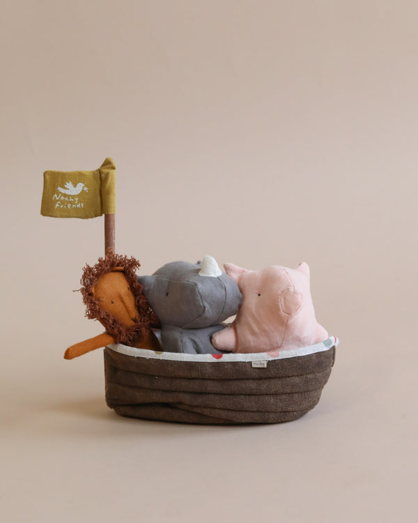 Noah's Friends Stuffed Animals are nestled together in a small, brown wicker basket. A tiny flag proclaims "Adventures await." Soft, neutral background enhances the warm, inviting.