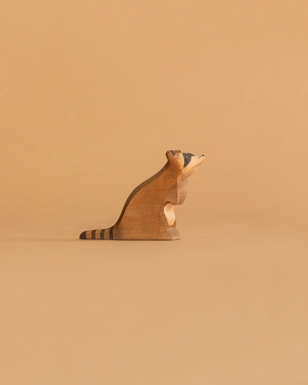 The Ostheimer Raccoon - Sitting is a small, handcrafted wooden figurine with a striped tail, shown on a beige surface and background—ideal for imaginative play and inspired by classic Ostheimer toys.