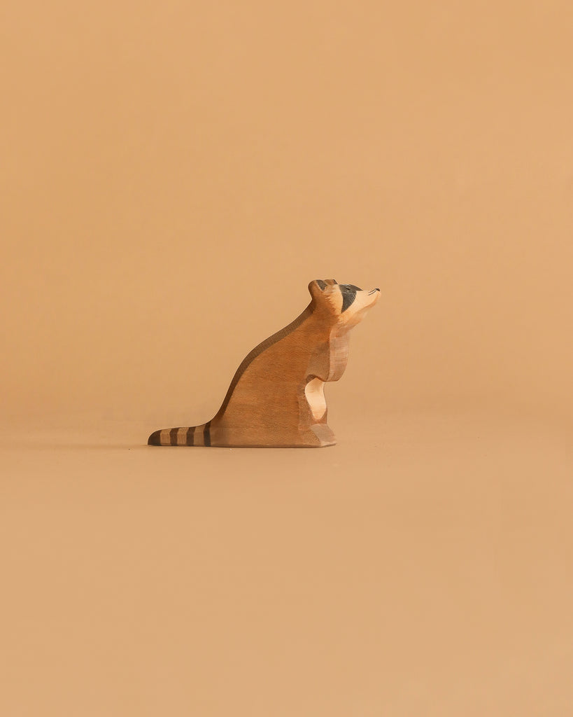 The Ostheimer Raccoon - Sitting is a small, handcrafted wooden figurine with a striped tail, shown on a beige surface and background—ideal for imaginative play and inspired by classic Ostheimer toys.