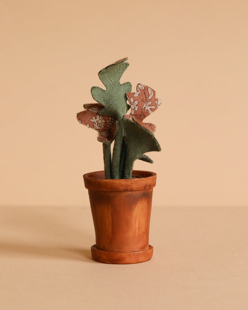 The Maileg Cozy Corner Set features a small terracotta pot with a plant that has green and floral-patterned fabric leaves, set against a beige background—perfect for pairing with the Maileg Vintage Floor Lamp to complete a charming miniature scene.