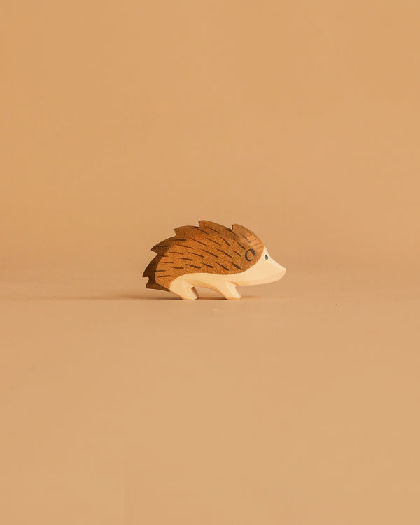 The Ostheimer Hedgehog is a small, simple wooden figurine in brown and beige, displayed on a tan surface with a matching background—ideal for imaginative play or as part of handcrafted wooden toy collections.