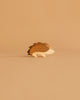 The Ostheimer Hedgehog is a small, simple wooden figurine in brown and beige, displayed on a tan surface with a matching background—ideal for imaginative play or as part of handcrafted wooden toy collections.