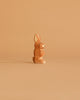 A light brown rabbit from the Ostheimer Handmade Wooden Woodland Set sits upright on a plain, solid beige background.