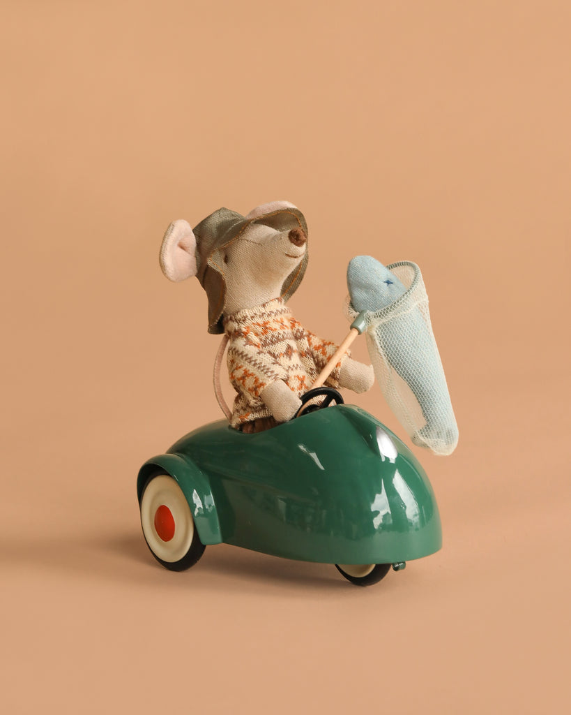 The Maileg Big Brother Gone Fishing Set features a small mouse in a hat and sweater, sitting in a green car and holding a net with a blue plush fish inside, set against a plain beige background.