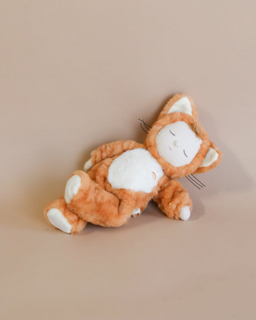 The Olli Ella Cozy Dinkum Doll - Tabby Cat Jinx, designed to look like a sleeping orange tabby cat named Jinx, features closed eyes, a white belly, and white paws. It lies on its side against a plain beige background with stitched-on whiskers and upright ears, adding to its charming appeal. Ships in approximately one week.