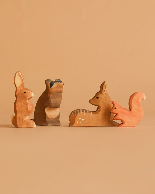 Four handcrafted figures from the Ostheimer Handmade Wooden Woodland Set—a rabbit, raccoon, deer, and fox—are arranged on a beige surface with a matching background. Made from sustainably sourced wood.
