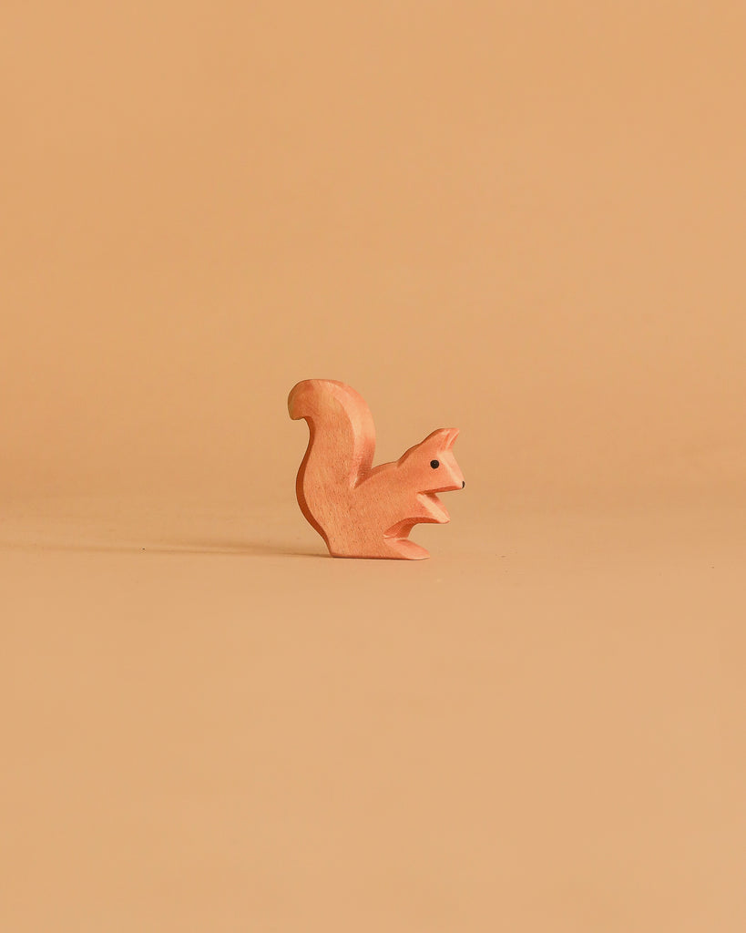 A small squirrel figurine from the Ostheimer Handmade Wooden Woodland Animals Set sits on a plain, light brown background, its minimalist wooden design blending subtly with its surroundings.