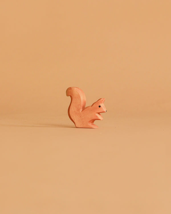 The Ostheimer Squirrel - Sitting is a small, handcrafted wooden figurine displayed on a plain light brown background, creating a minimalist look that inspires imaginative play.