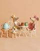 Two Maileg Ballerina Mice in dresses sit at a small table having tea with the Maileg Afternoon Tea Set, which includes cups, cakes, and macarons. The background is a plain beige.
