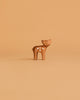 A small, brown deer figurine with white spots stands on a plain, light brown background, reminiscent of the Ostheimer Handmade Wooden Woodland Set.