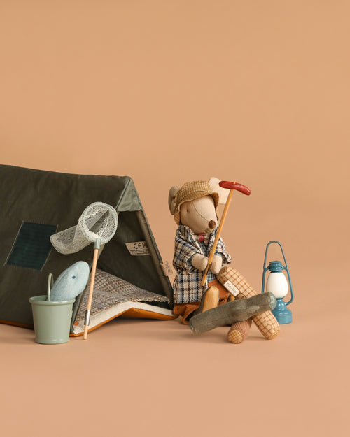 The Maileg Camping Set with Granddad features a toy mouse in a plaid coat by a cozy tent, holding a red-handled tool. Classic accessories—like a butterfly net, bucket with toy fish, blue lantern, and campfire—complete the beige background scene.