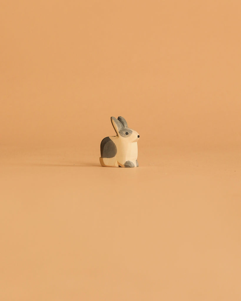 The Ostheimer Black & White Rabbit - Sitting is a charming figurine on a peach background, ideal for sparking imaginative play and pairing perfectly with other Ostheimer toys.