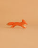 The Ostheimer Fox - Running, a minimalist wooden fox figurine painted orange with white details, is displayed against a matching light orange background.