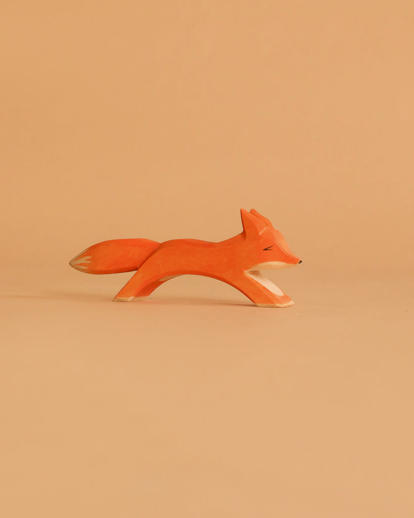 The Ostheimer Fox - Running, a minimalist wooden fox figurine painted orange with white details, is displayed against a matching light orange background.