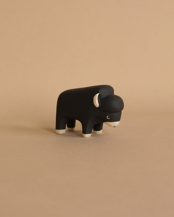 A handmade tiny wooden bison with white details on a beige background, hand-carved by artisans in Indonesia, positioned centrally with a side profile view.