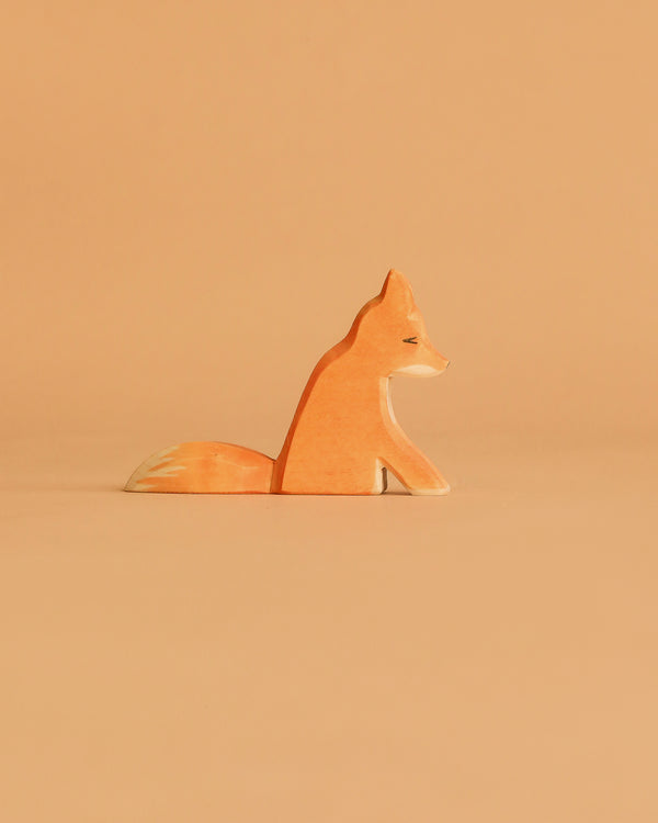 The Ostheimer Fox - Sitting is a small handcrafted wooden figurine, painted in orange and white hues, ideal for imaginative play and displayed against a light brown background.