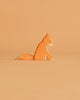 The Ostheimer Fox - Sitting is a small handcrafted wooden figurine, painted in orange and white hues, ideal for imaginative play and displayed against a light brown background.