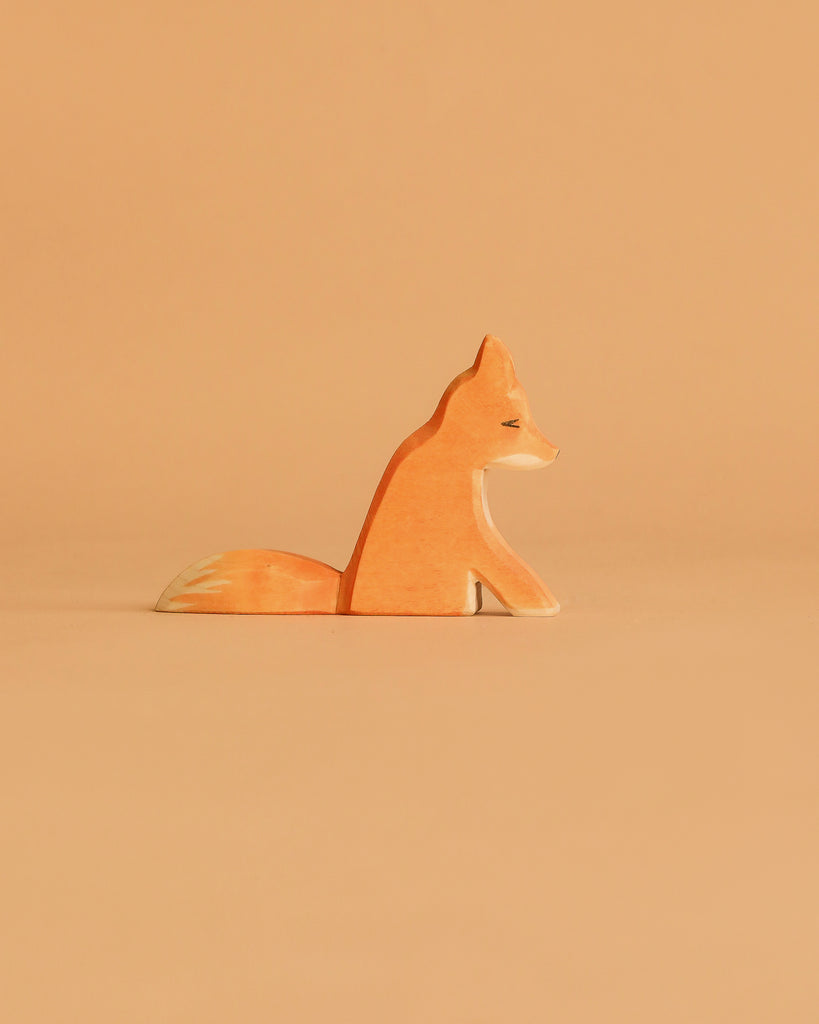 The Ostheimer Fox - Sitting is a small handcrafted wooden figurine, painted in orange and white hues, ideal for imaginative play and displayed against a light brown background.