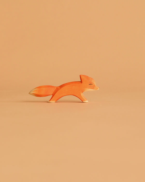 The Ostheimer Small Fox - Running is a minimalist wooden figurine in orange and white, shown on a light orange background—ideal for imaginative play or to add to your handcrafted wooden toys collection.