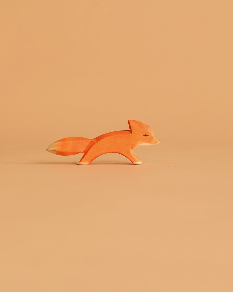 The Ostheimer Small Fox - Running is a minimalist wooden figurine in orange and white, shown on a light orange background—ideal for imaginative play or to add to your handcrafted wooden toys collection.