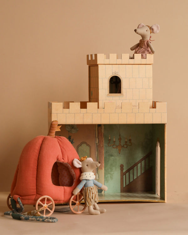 In the Maileg Fairytale Set, a plush mouse perches on a turret of the cardboard castle, while another stands next to a pumpkin-shaped carriage. The whimsical scene is beautifully offset by the beige background.