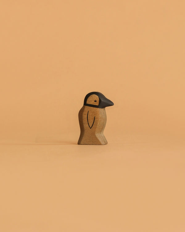 The Handmade Holzwald Penguin, Small, features a carved wooden body with a black beak and head, standing upright on a light orange background—a delightful addition to any sustainable wooden toy collection or for imaginative play.