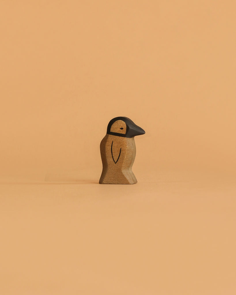 The Handmade Holzwald Penguin, Small, features a carved wooden body with a black beak and head, standing upright on a light orange background—a delightful addition to any sustainable wooden toy collection or for imaginative play.