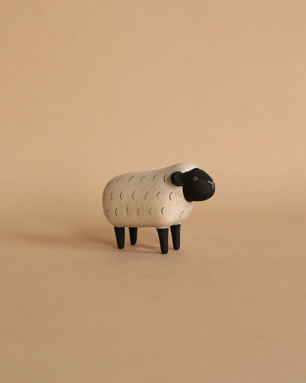 A small, decorative Handmade Tiny Wooden Farm Animals - Sheep figurine handcrafted from Albizia wood with a textured body and black head stands against a plain beige background.