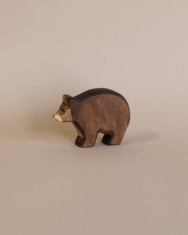 A Handmade Holzwald Bear on a plain beige background. The bear is dark brown with lighter accents on its face and body, standing in profile, colored with natural dyes.
