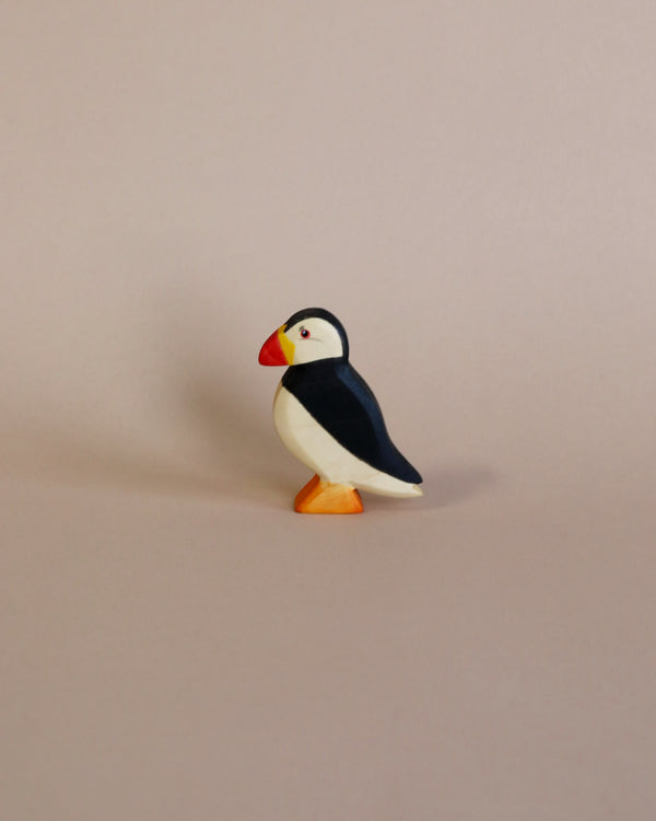 A Handmade Holzwald Puffin Bird figurine with black, white, and orange colors, standing on an orange base set against a light pink background. This educational toy enhances learning through nature-inspired play.