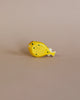 A small, yellow, wooden fish figurine with black spots and a white tail rests on a beige surface and background—part of the Handmade Holzwald Underwater World Set.