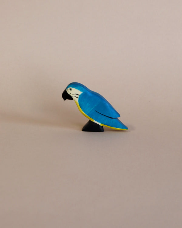 A Handmade Holzwald Blue Parrot painted in vibrant blue and yellow, positioned to the left on a plain light beige background. This educational toy is designed to stimulate creativity and learning.