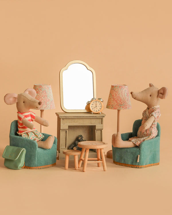 The Maileg Mother & Daughter Living Room Set features two mice on teal furniture with a table, mantle, mirror, and clock between them. The cozy scene has a pastel aesthetic against a beige background.