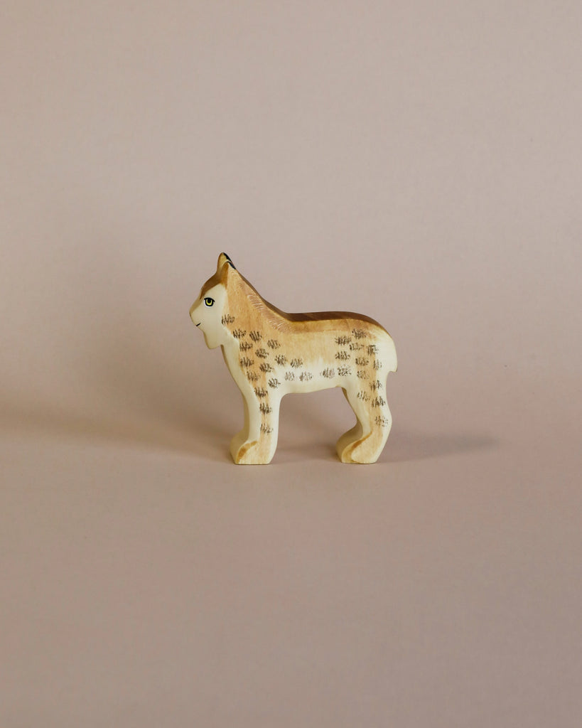 A small, hand-carved Handmade Holzwald Lynx with painted details stands against a plain beige background. Crafted by the Holzwald Brand, the figure is light brown with distinctive dark spots and markings, embodying the brand’s commitment to sustainable toys.