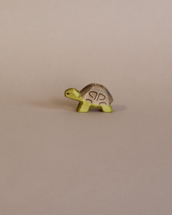 A small figurine of a Handmade Holzwald Small Turtle, featuring a metallic, patterned shell and a green body, standing against a plain light background.