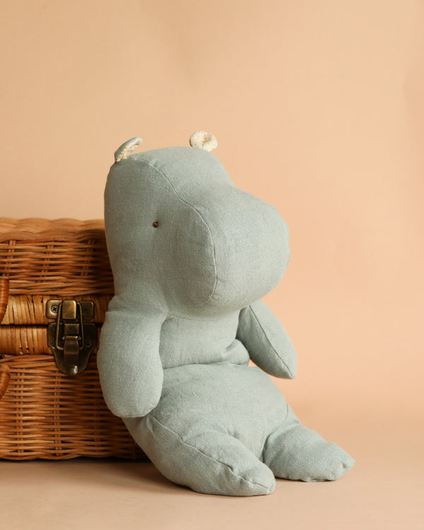 A soft, blue Maileg Medium Hippo stuffed animal with white ears sitting against a woven basket on a plain beige background. This adorable stuffed animal is part of our "Safari Friends" collection.