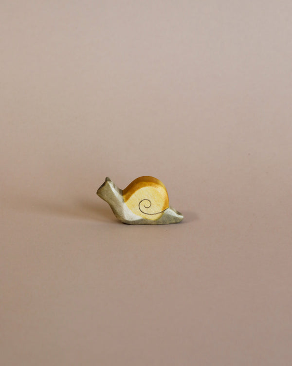 A Handmade Holzwald Small Snail with a shiny gold shell and a matte white body, positioned on a smooth light tan background by Holzwald Brand.