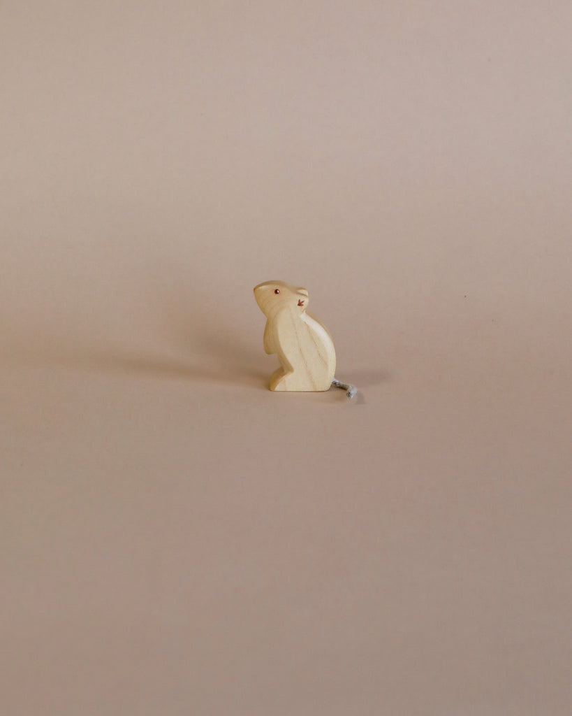 A small, simple wooden mouse figurine, crafted from sustainable toys materials, standing upright on a plain beige background, casting a soft shadow to its right.