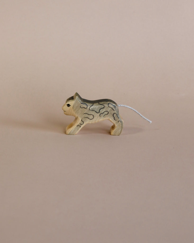 A Handmade Holzwald Small Snow Leopard with a striped pattern and a white, string tail, standing on a plain beige background. This educational toy promotes learning through play.
