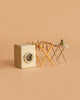 The Maileg Laundry Room Set, featuring a miniature washing machine, drying rack with tiny clothes, and a small ironing board with iron, is displayed on a peach-colored background.