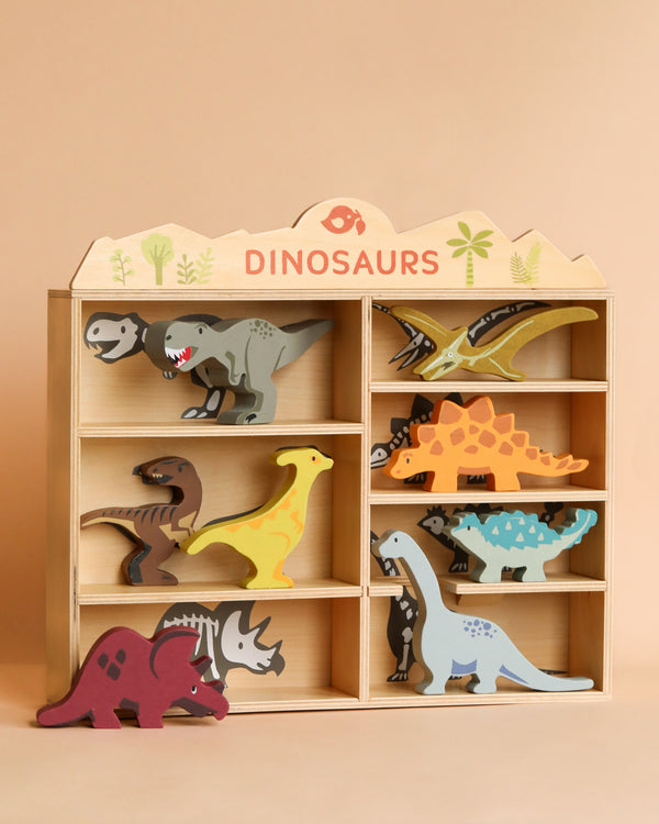 Wooden display shelf labeled "Dinosaurs Set" containing colorful sustainably sourced toys in various poses, set against a plain beige background.