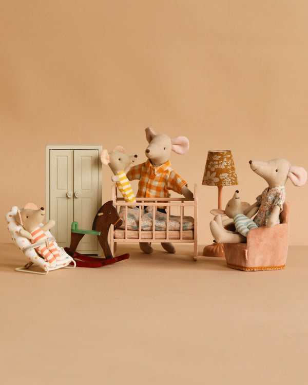 The Maileg Nursery Set With Mice features Mum Mouse and three baby triplets in a beige nursery with a crib, rocking chair, and dollhouse furniture, creating a warm and playful bedtime scene.