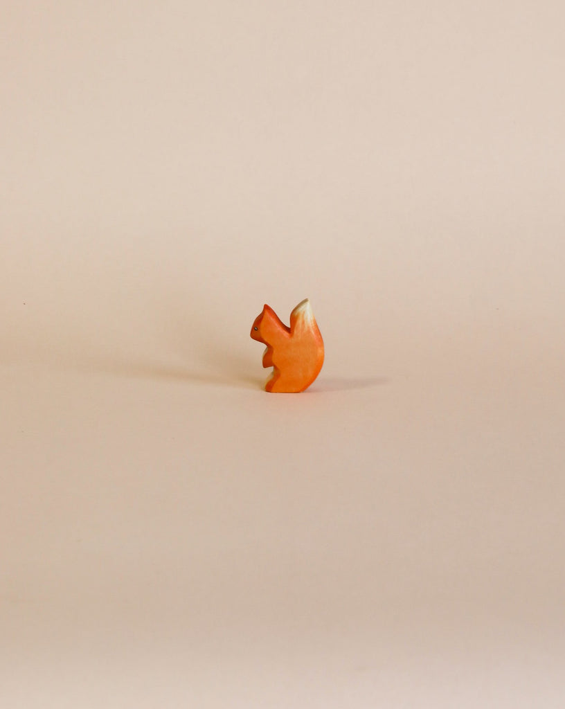 A small, uniquely shaped Handmade Holzwald Small Squirrel stands upright against a plain, light beige background, suggesting it could inspire sustainable toys.