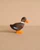 A brown Holztiger Handmade Wooden Animal Play Set duck toy, hand-carved with an orange beak/feet, white neck ring, and blue wing detail, highlights European craftsmanship against a plain beige background.
