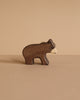 A small, brown bear figurine with a white snout from the Holztiger Handmade Wooden Woodland Animals Set stands on a beige surface against a matching background—a charming example of classic wooden animal toys.