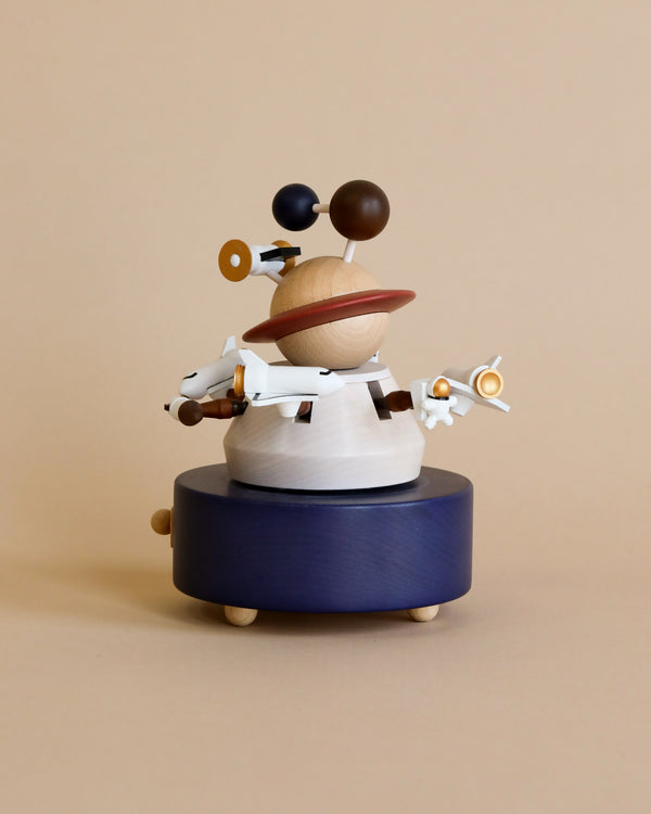 A whimsical Wooden Outer Space Music Box featuring abstract shapes and forms, including spheres and a propeller, mounted on a circular navy blue base against a light beige background.