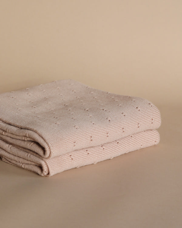 A neatly folded apricot handmade Merino wool Bibi blanket displayed against a plain beige background. The blanket has a pattern of small, raised dots and is suitable for sensitive skin.